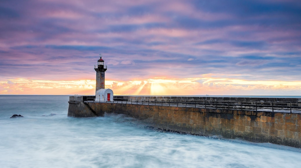 A lighthouse by the sea with a sunset in the background.