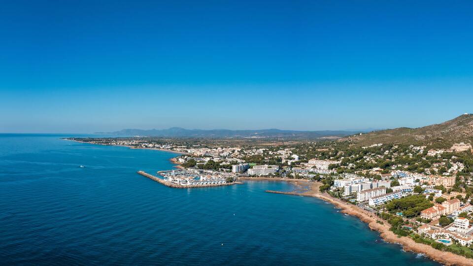 A coastal town with a marina, buildings, and a mountainous backdrop.