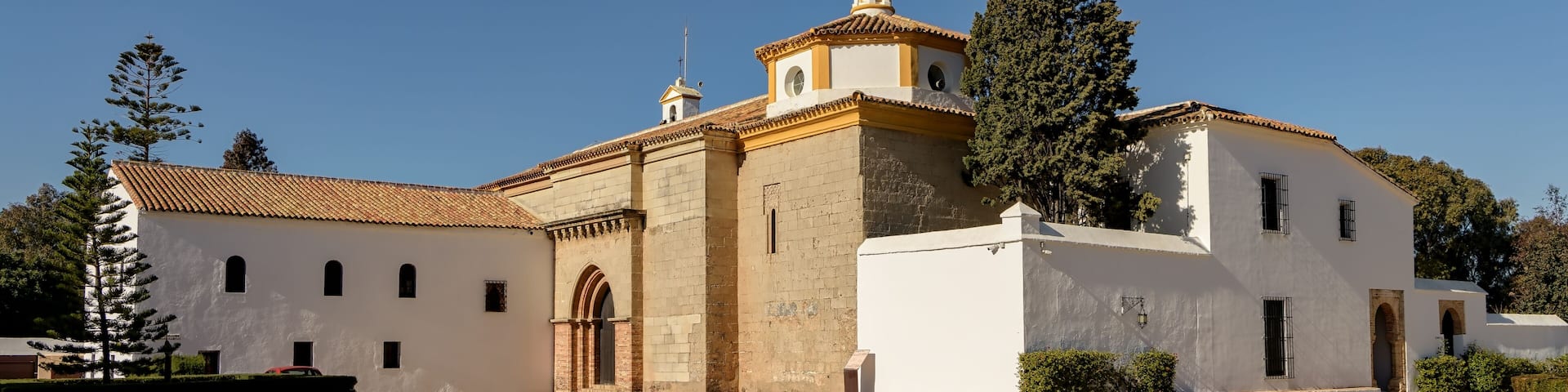 A historic church with a bell tower, surrounded by trees and a clear sky.