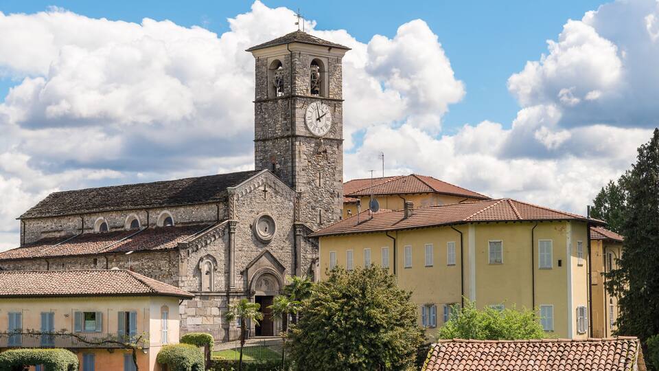A historic church with a clock tower, surrounded by traditional buildings and lush gardens.