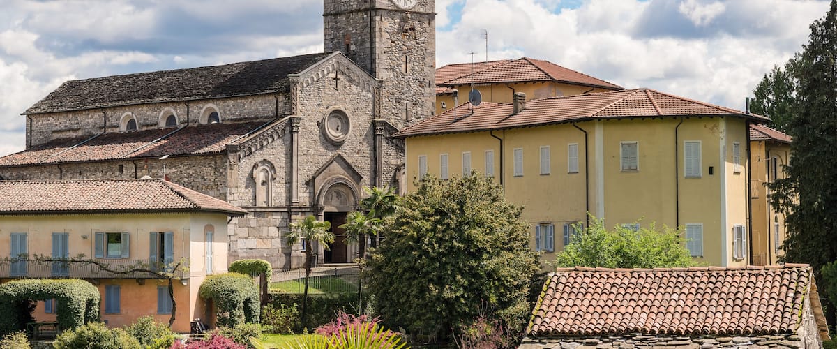 A historic church with a clock tower, surrounded by traditional buildings and lush gardens.