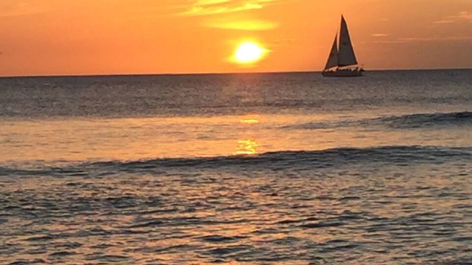 A sunset over the ocean with a sailboat in the distance.