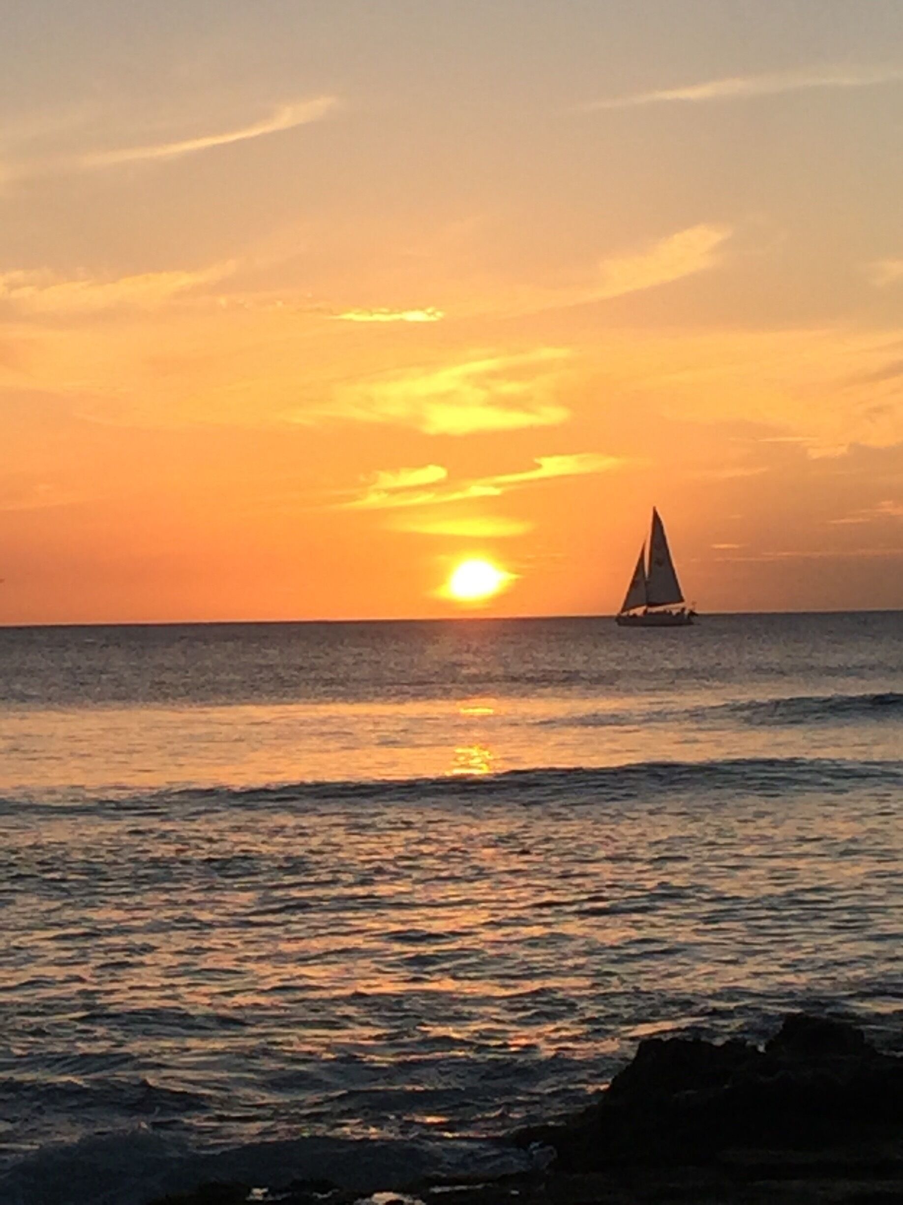 A sunset over the ocean with a sailboat in the distance.