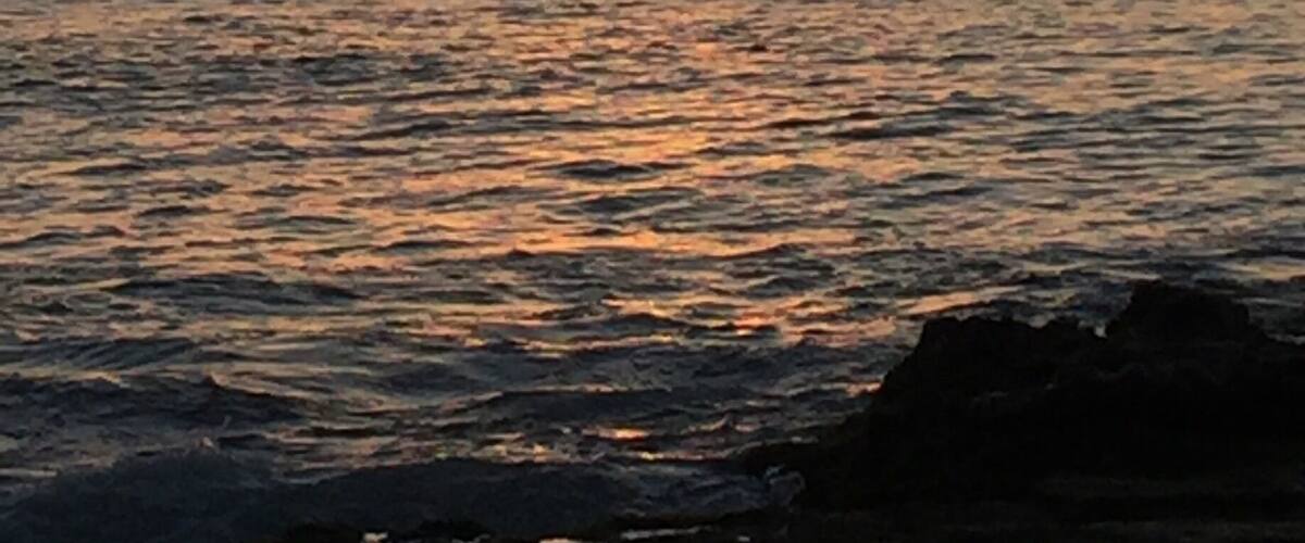 A sunset over the ocean with a sailboat in the distance.