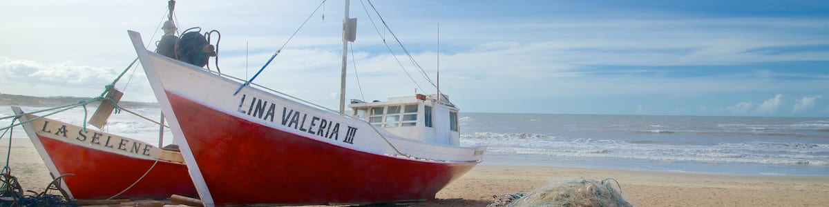 A red and white boat named 'LINA VALERIA III' on a sandy beach with the ocean in the background.
