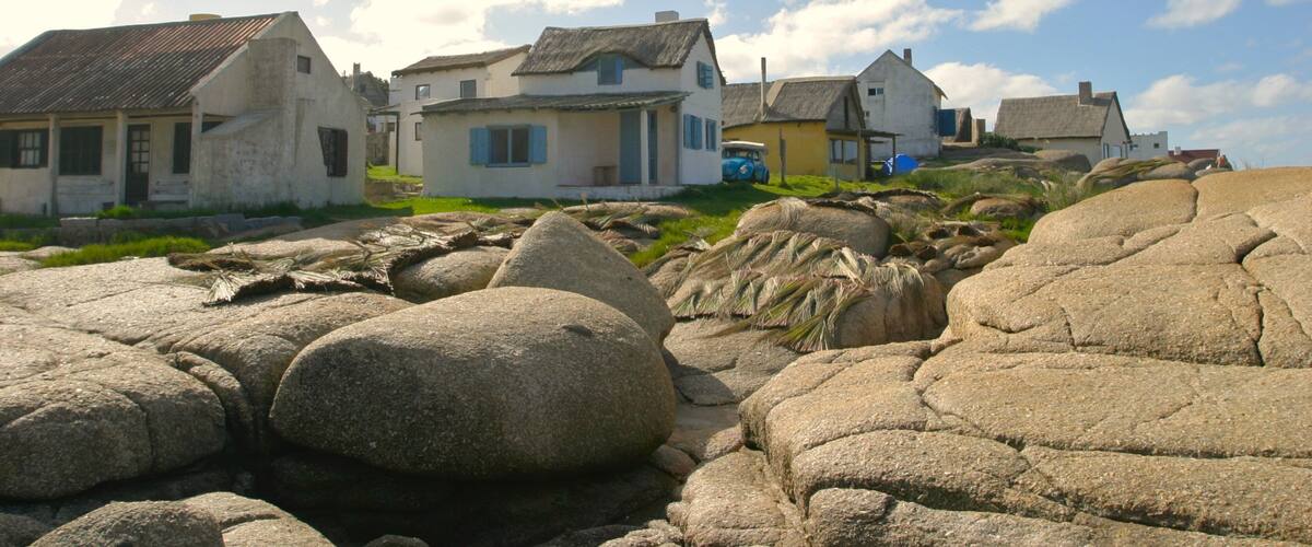 A coastal village with thatched-roof houses and large boulders.