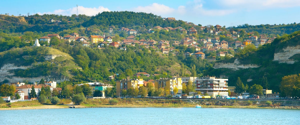 A coastal town with buildings on a hillside, a body of water in the foreground, and a clear sky.