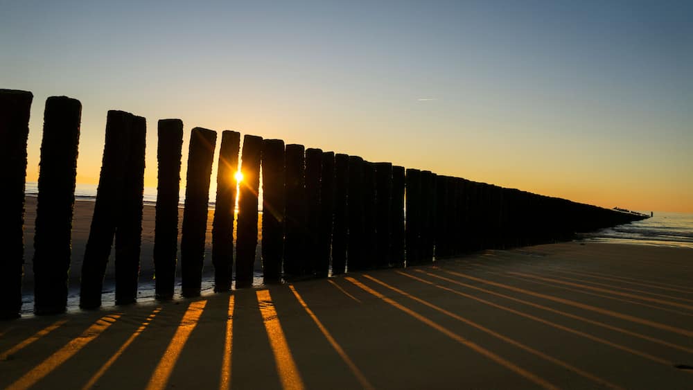 Une plage avec des poteaux en bois et le soleil se couchant à l’horizon.