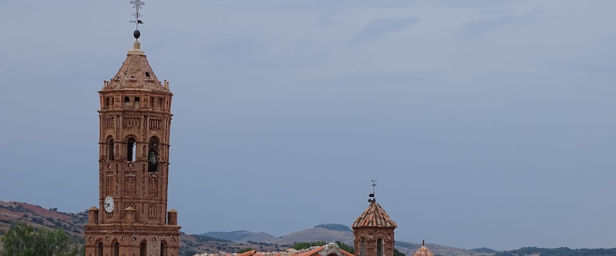 A historic church with a tall bell tower and a smaller dome, surrounded by traditional red-tiled roofs and brick buildings.