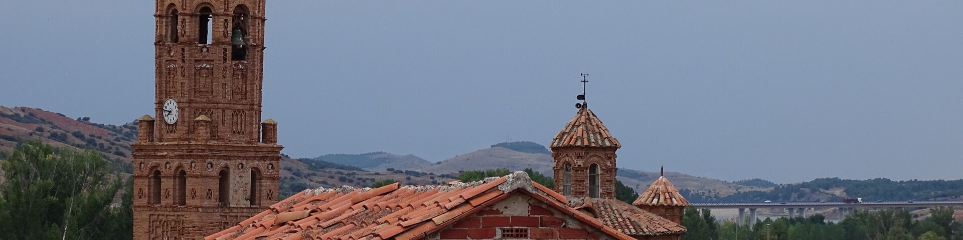A historic church with a tall bell tower and a smaller dome, surrounded by traditional red-tiled roofs and brick buildings.