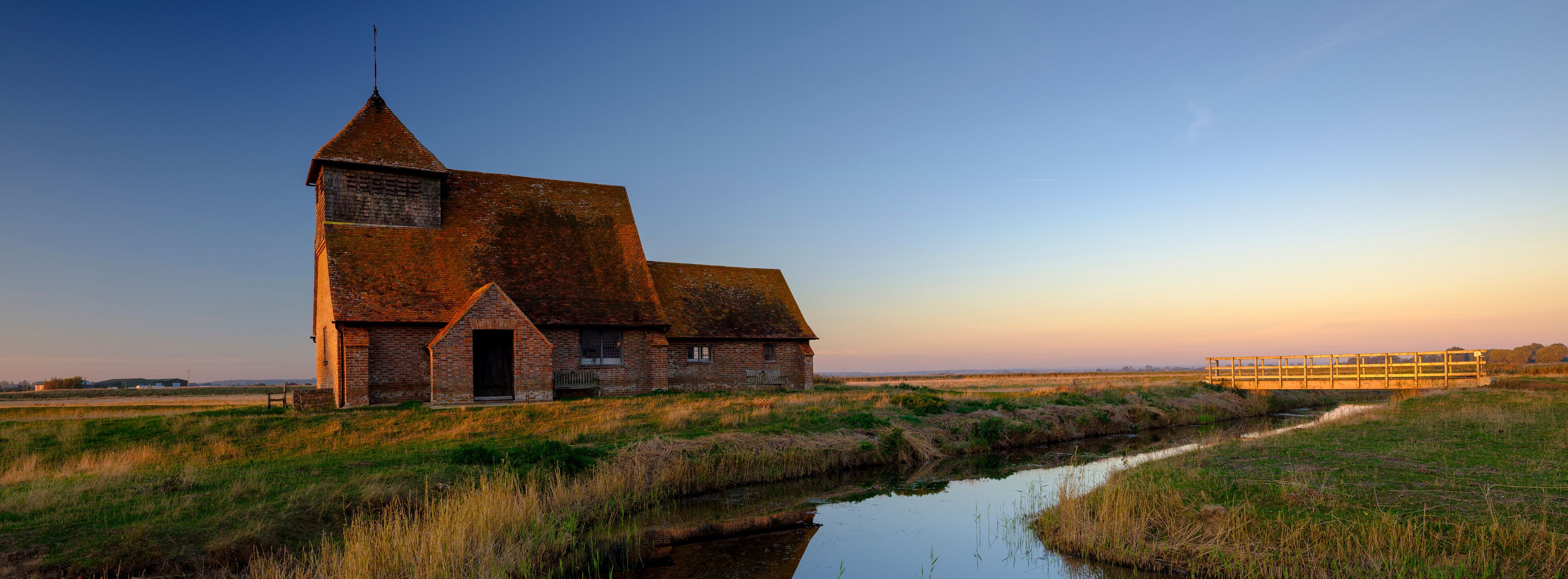 A brick church with a tower and a wooden bridge over a canal.