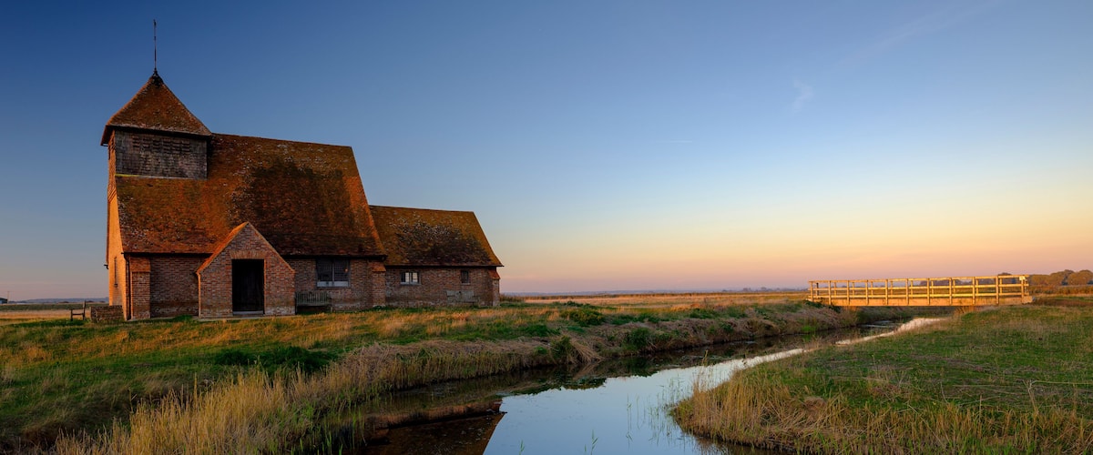 A brick church with a tower and a wooden bridge over a canal.