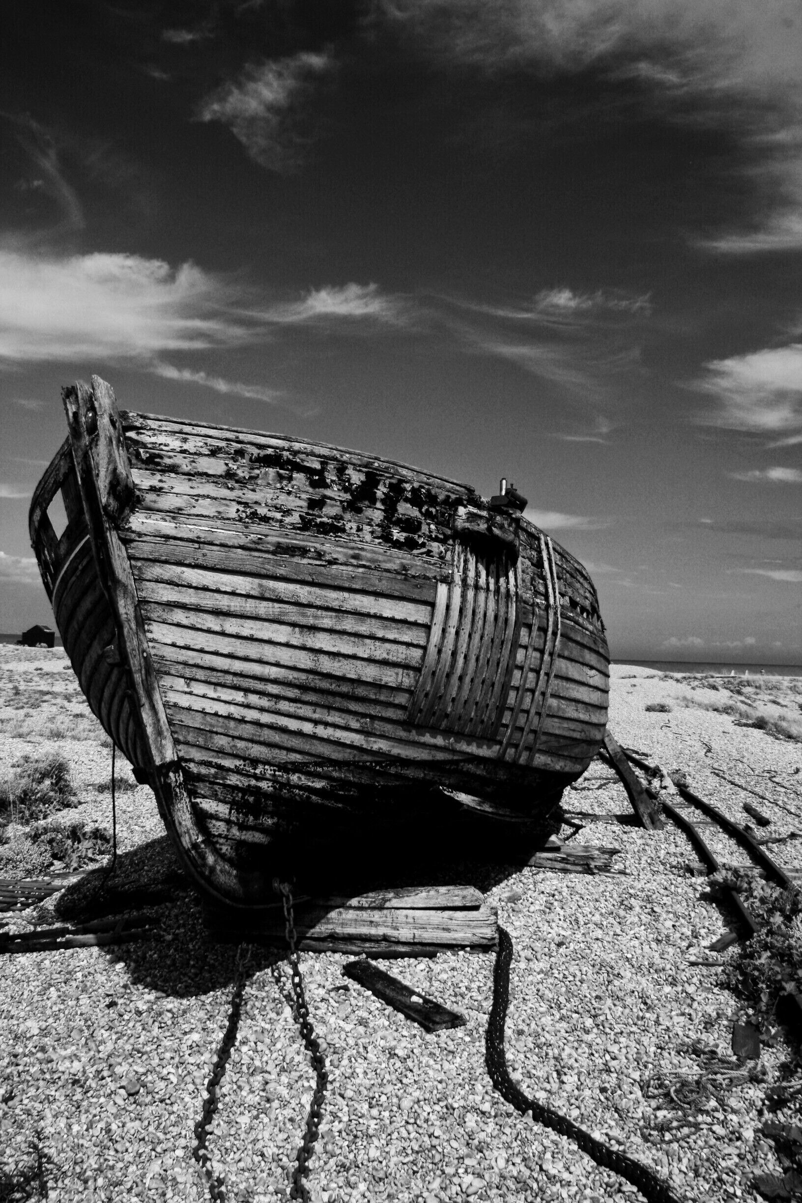 A derelict wooden boat on a sandy beach with a clear sky.