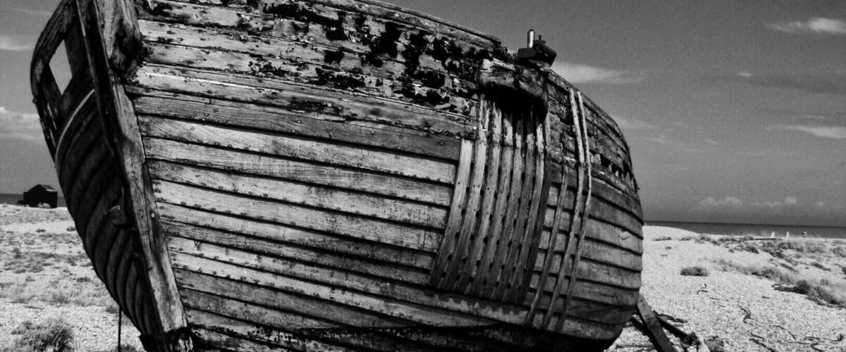 A derelict wooden boat on a sandy beach with a clear sky.
