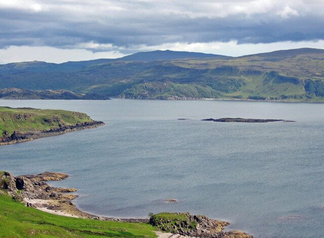 A coastal landscape with a large body of water, green hills, and rocky shores.