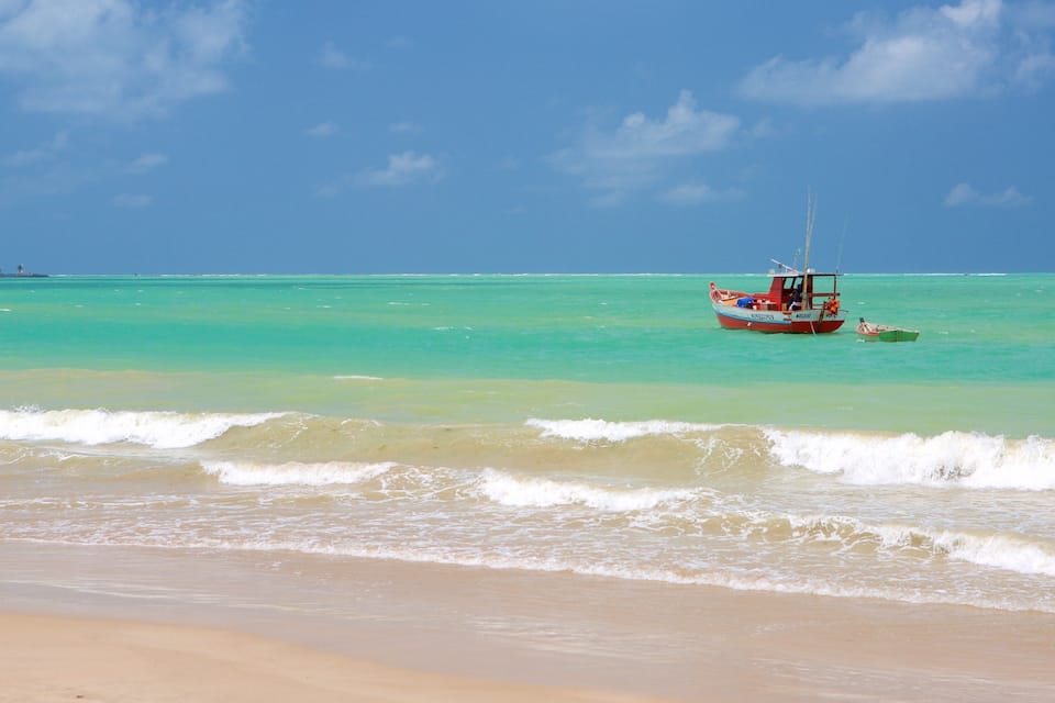 A beach with turquoise water, a boat, and a clear sky.