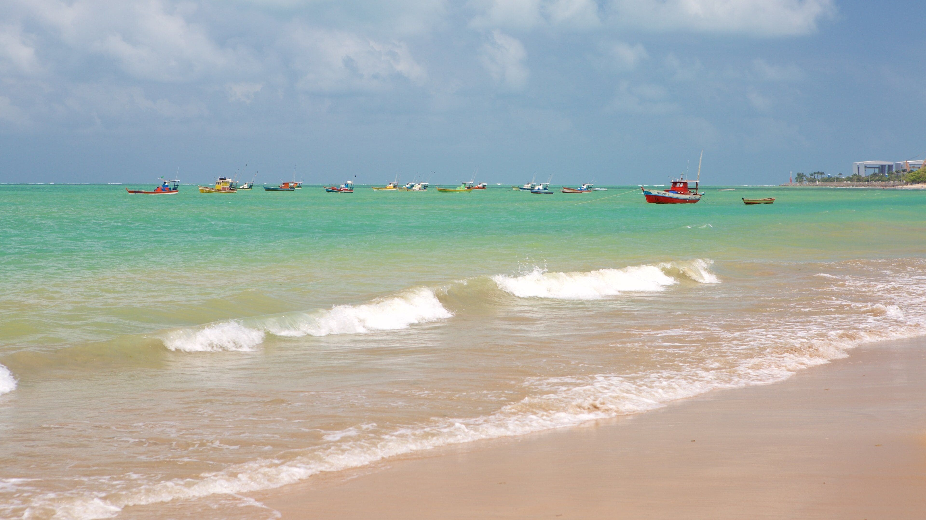 Une plage avec une eau turquoise, des vagues et plusieurs bateaux.