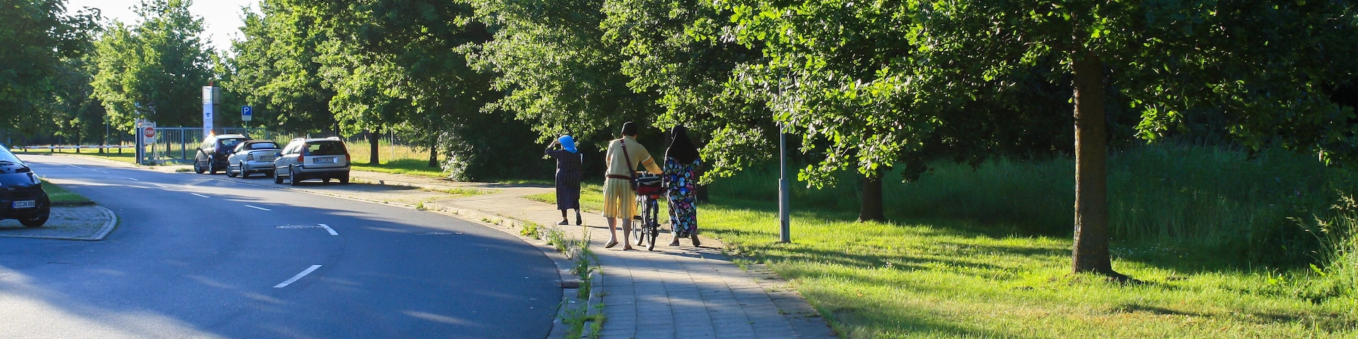 View of park and empty road with people on sidewalk in Itzehoe, Germany with bright sunny sky background.