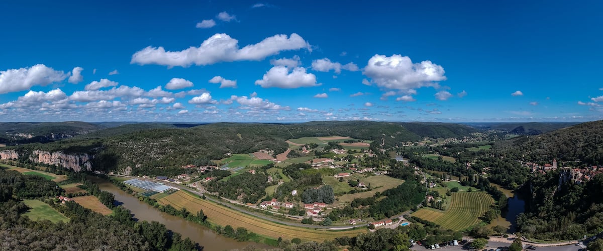 A panoramic view of a valley with a river, fields, and a town surrounded by hills and cliffs.