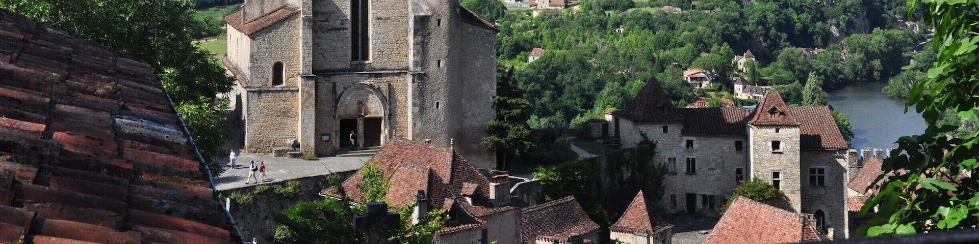 A historic stone tower with a red roof, surrounded by lush green hills and a river.