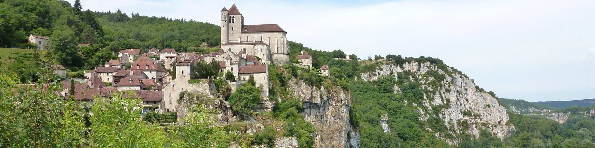 A historic castle on a cliff overlooking a river, surrounded by lush greenery.