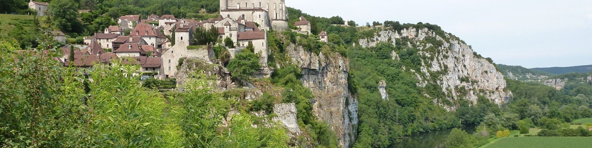 Um castelo histórico numa falésia com vista para um rio, rodeado por vegetação exuberante.