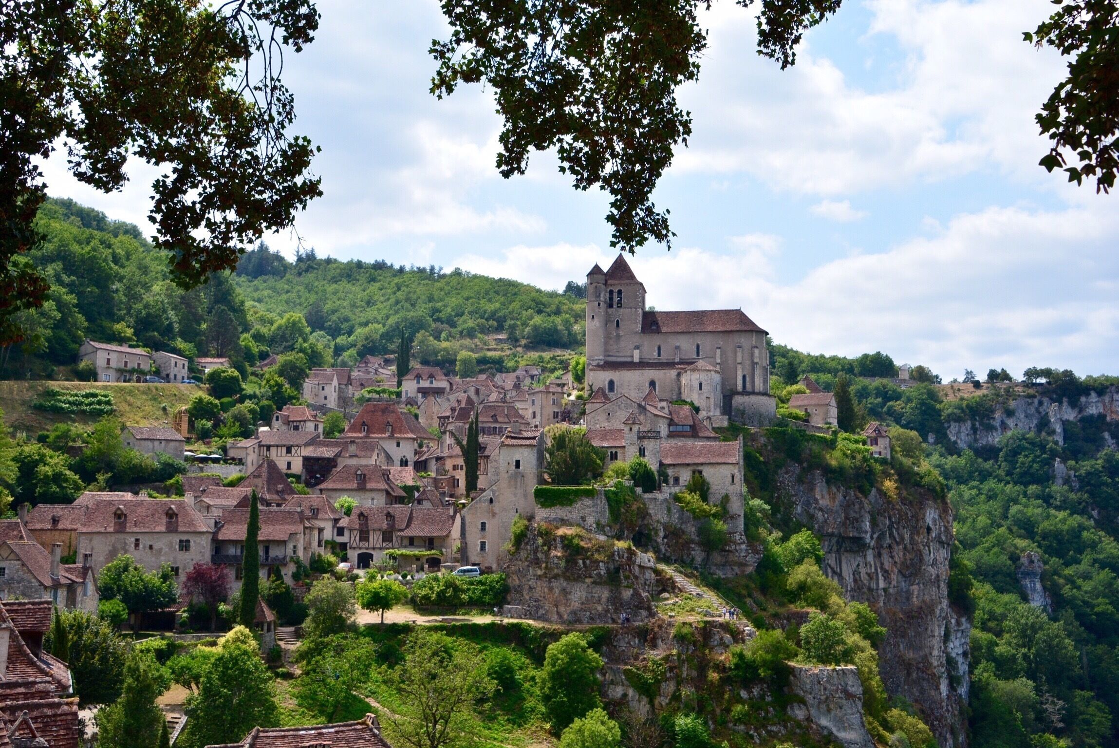 A medieval town perched on a cliff, surrounded by lush greenery and historic buildings.