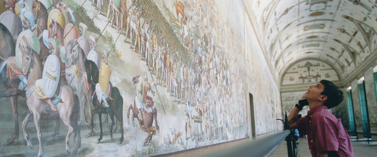 A person standing in front of a large mural depicting a historical battle scene.