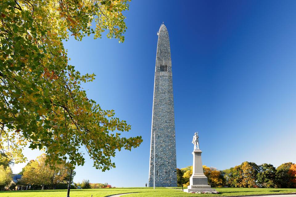 Un alto monumento obelisco circondato da un parco con foglie autunnali.
