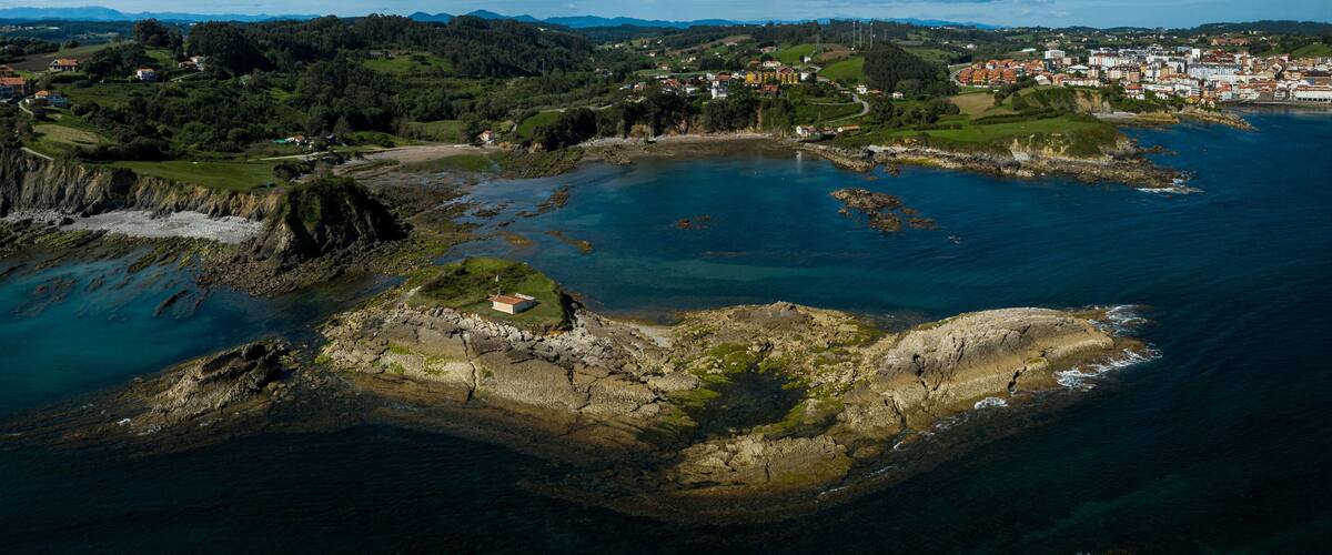 An aerial view of a coastal town with a rocky shoreline, a small island with a building, and a large body of water.