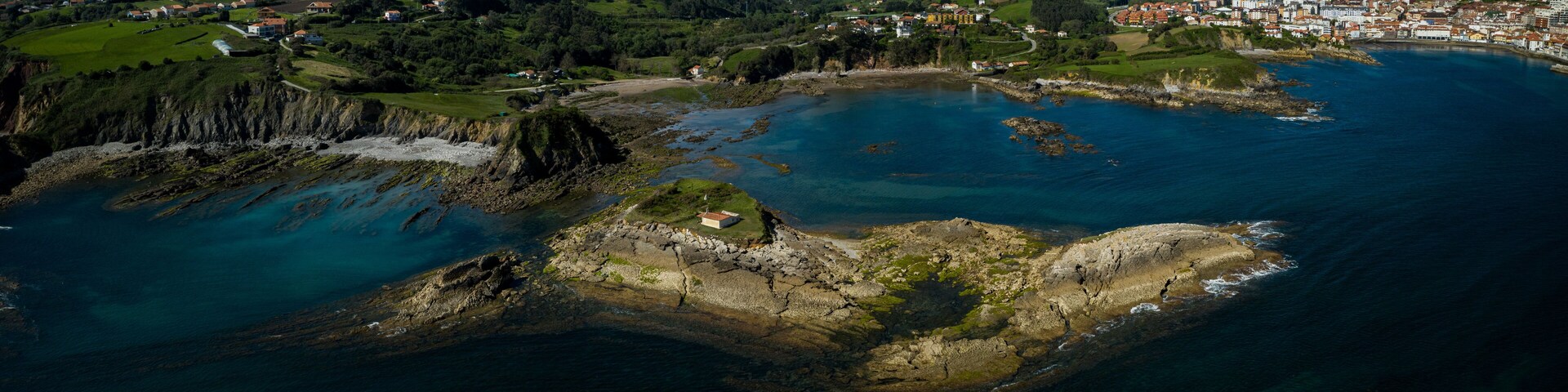 An aerial view of a coastal town with a rocky shoreline, a small island with a building, and a large body of water.