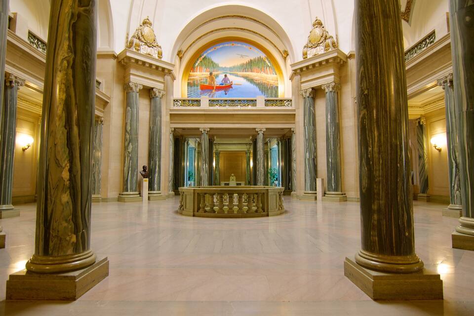 Un gran salón con columnas de mármol, una estatua central y un mural que representa un paisaje fluvial.