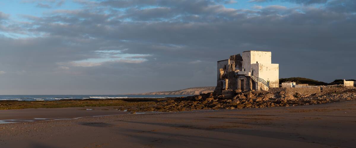A coastal ruin with a staircase leading up to a tower, surrounded by a rocky beach and ocean.