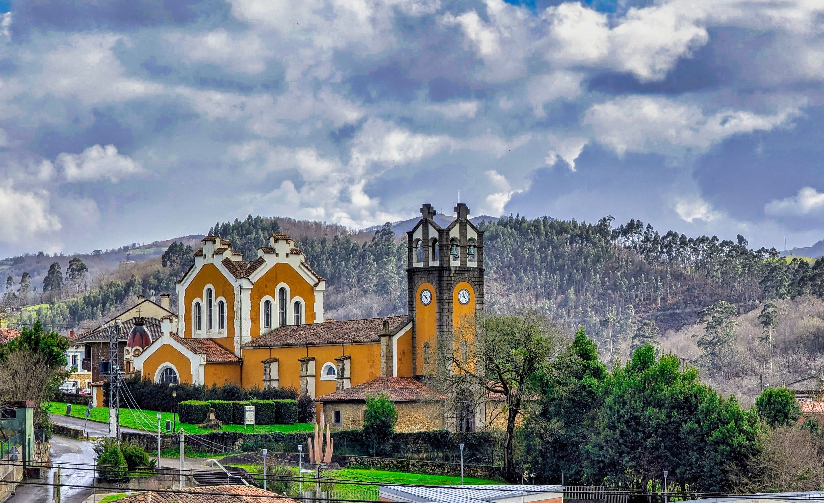 A church with a bell tower, surrounded by a green landscape and hills.