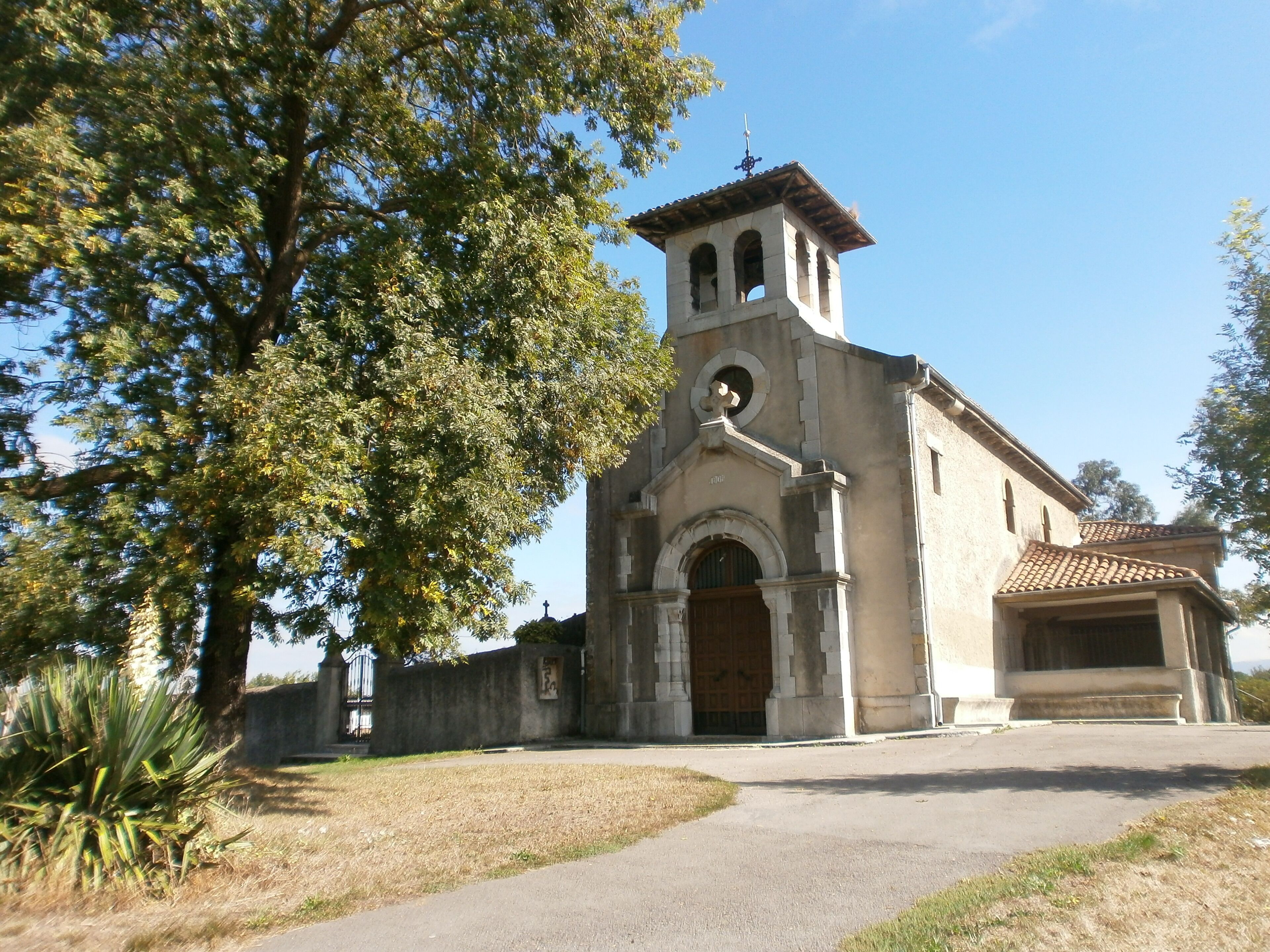 A church with a bell tower, surrounded by trees and a clear sky.