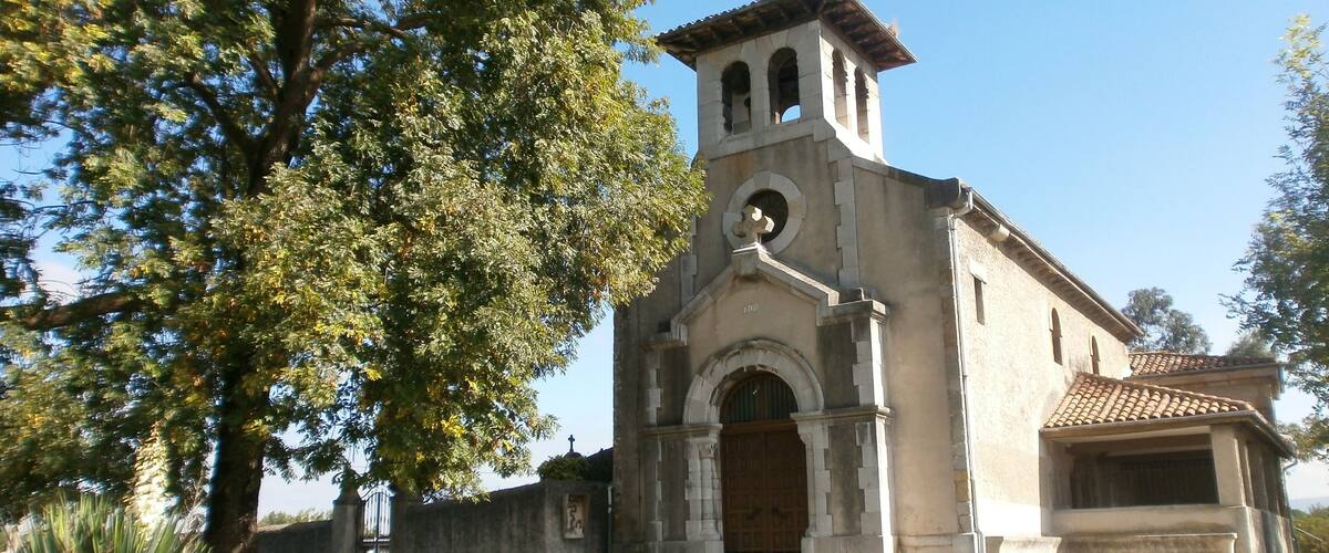 A church with a bell tower, surrounded by trees and a clear sky.