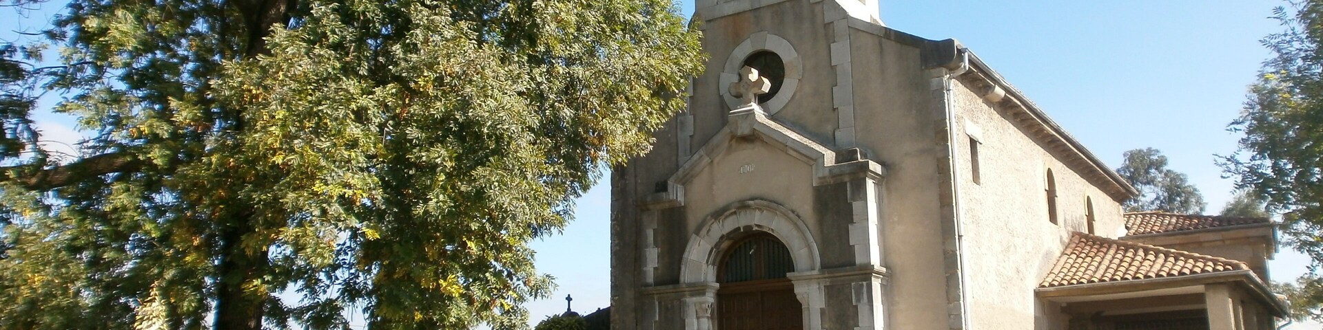 A church with a bell tower, surrounded by trees and a clear sky.
