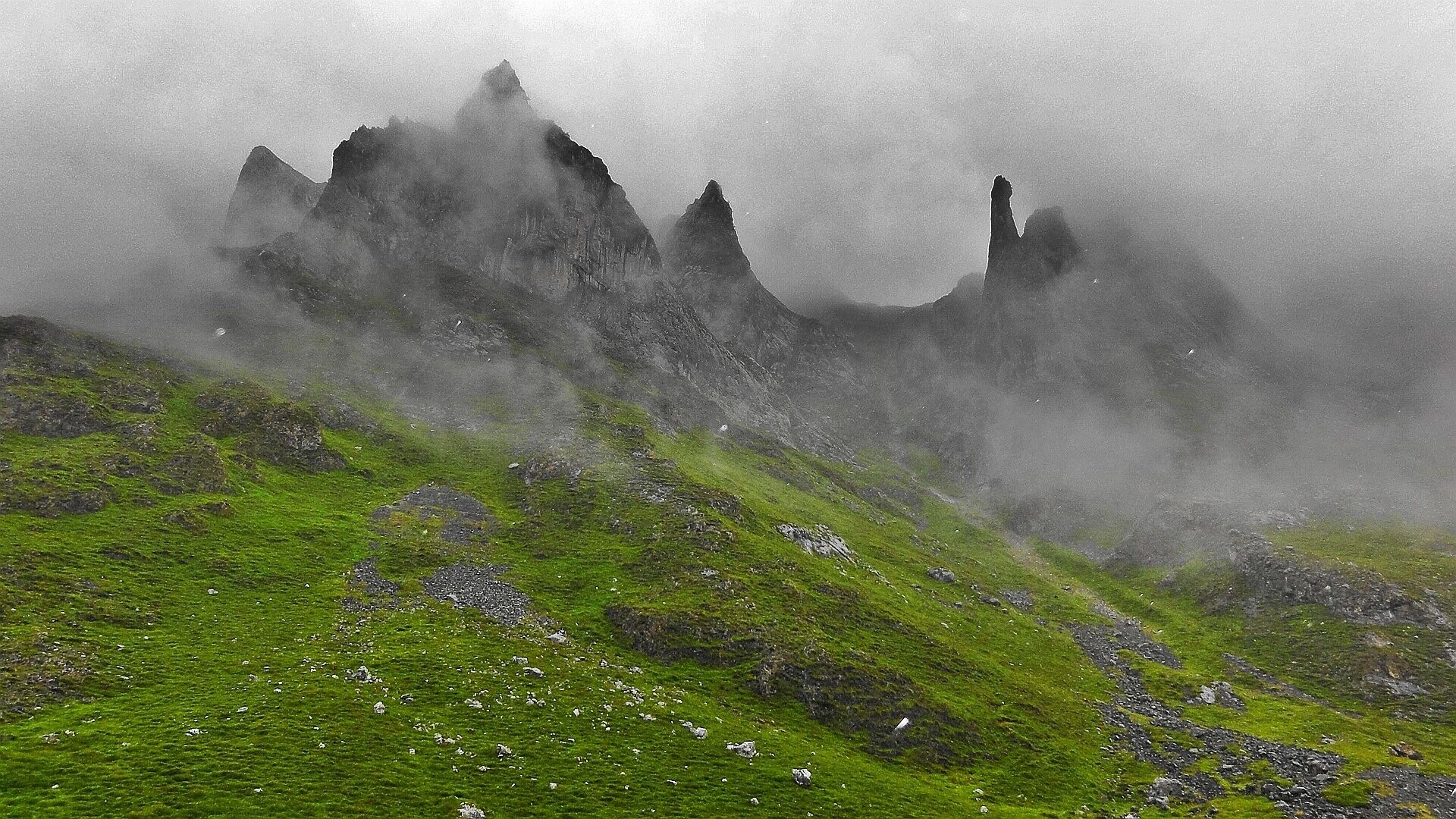 A mountainous landscape with green grass and rocky outcrops partially obscured by mist.