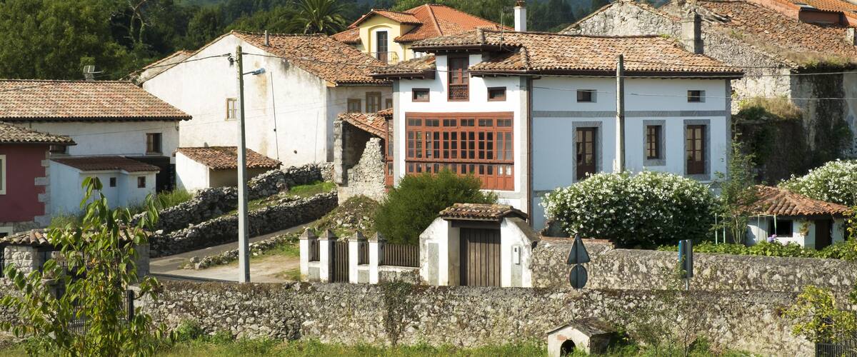 A village with traditional buildings, stone walls, and a mountainous backdrop.