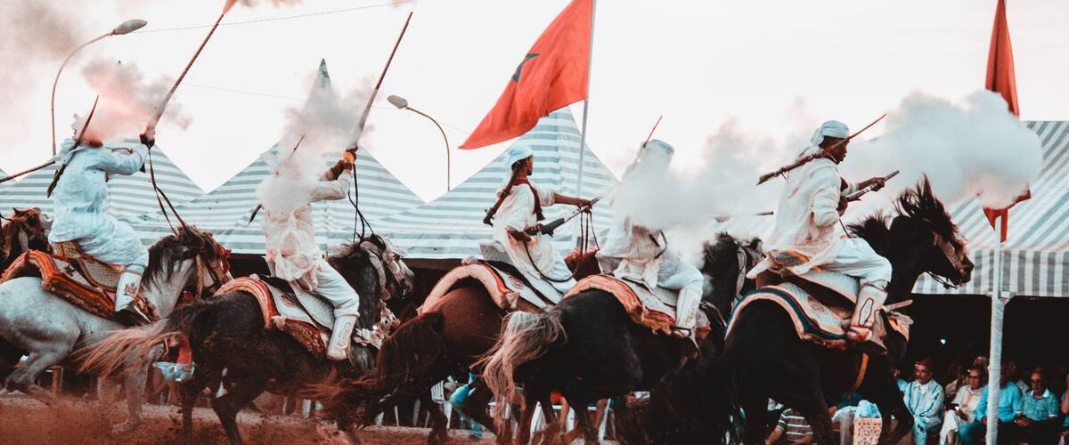 A historical reenactment with riders on horses, flags, and spectators.