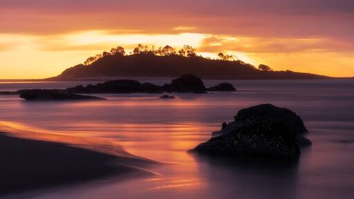 Panorama long exposure of an orange sunrise across a seascape scene of rocks looking out towards the silhouette of Green Island at Cunjurong Point, New South Wales Australia