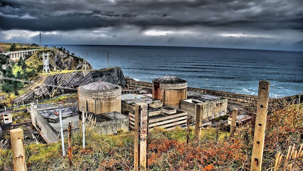 A coastal industrial site with large cylindrical structures and a bridge.