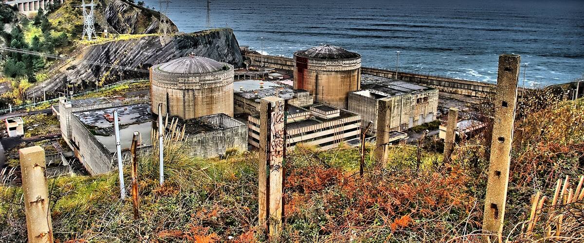 A coastal industrial site with large cylindrical structures and a bridge.