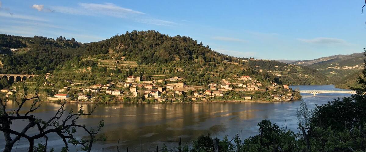 A riverside town with a bridge, surrounded by hills and vineyards.