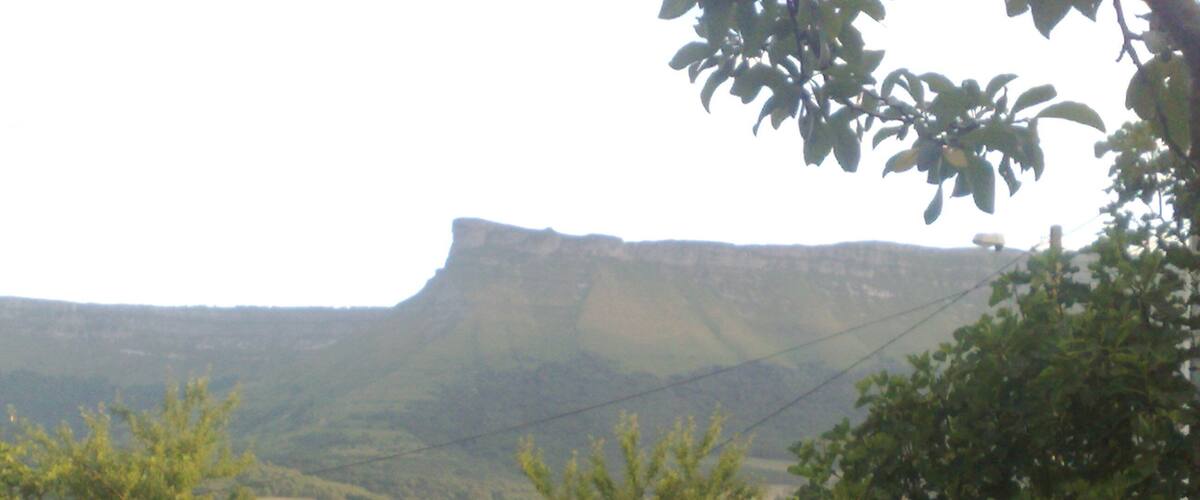 A mountainous landscape with a prominent cliff, trees, and a building in the foreground.