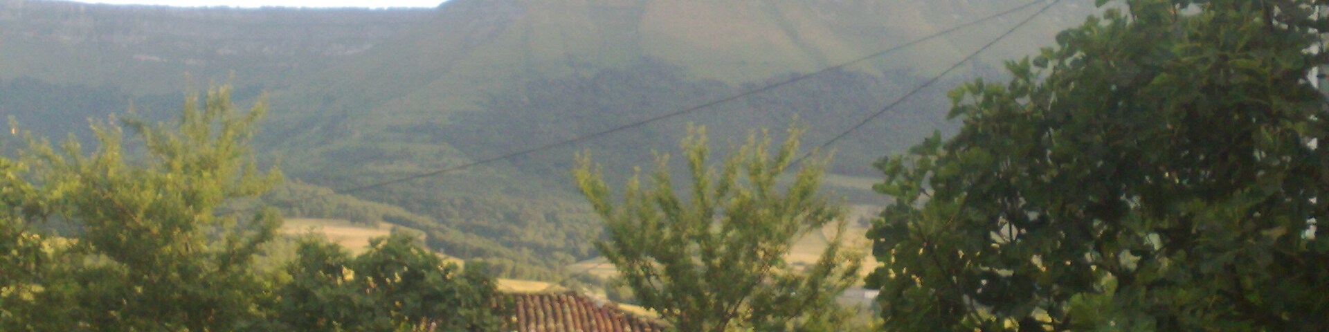 A mountainous landscape with a prominent cliff, trees, and a building in the foreground.