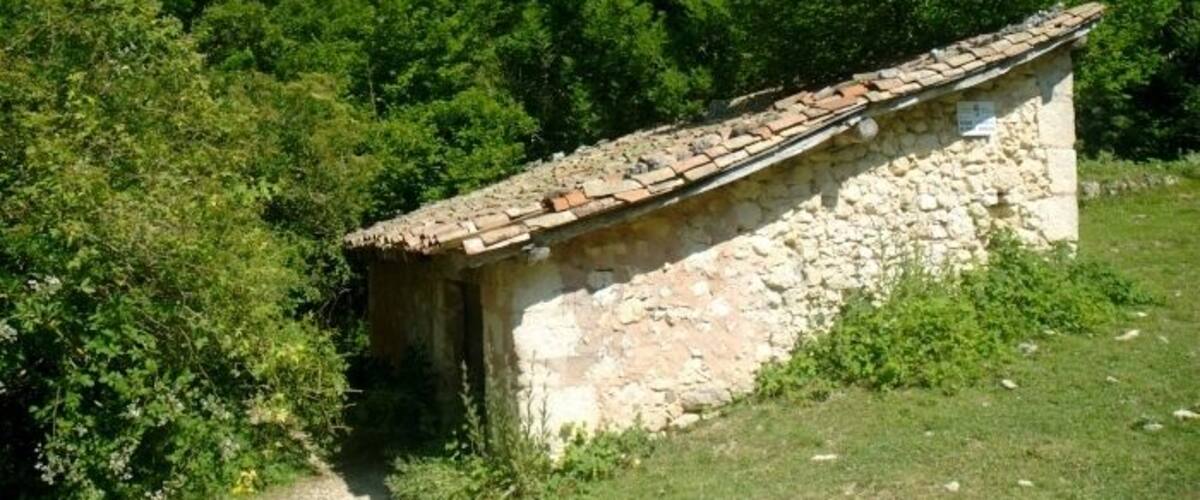 A stone building with a tiled roof surrounded by dense green trees and a rocky hillside.