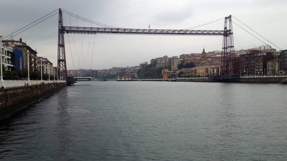 A large suspension bridge over a river with buildings on either side.