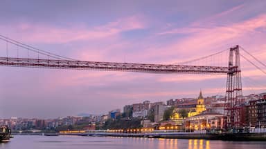 A red bridge spanning a river with city buildings on either side.