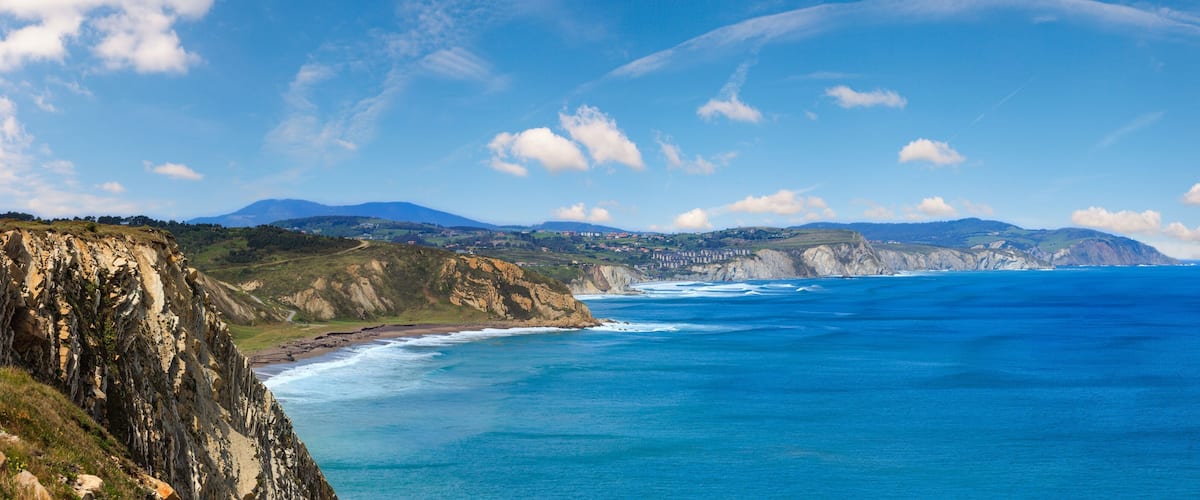 A coastal landscape with cliffs, a beach, and distant mountains under a clear sky.